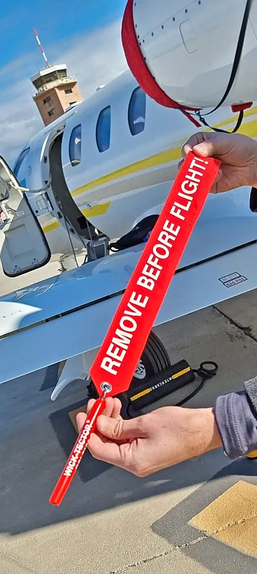 Aviation professional holding a red ‘REMOVE BEFORE FLIGHT’ safety cover at an airport.