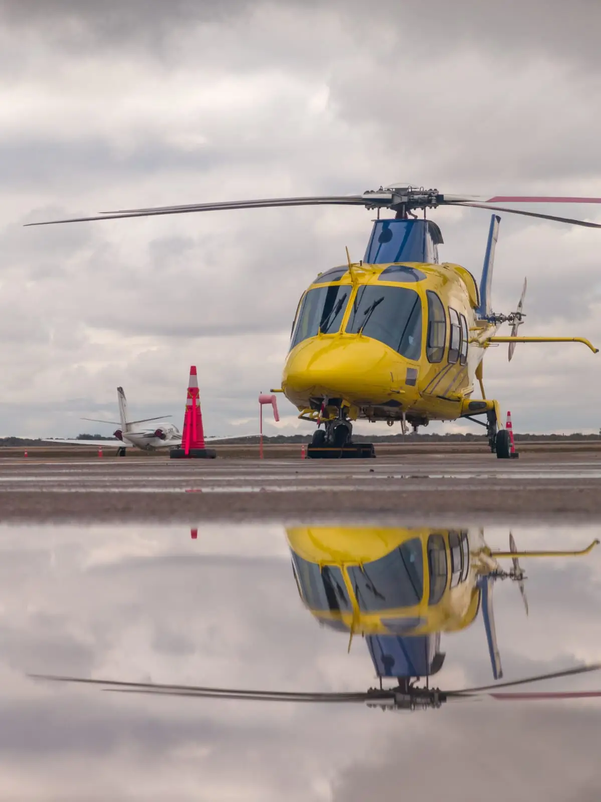 Helicopter reflected on wet tarmac during rain, waiting for takeoff with Agile Aero ground support.